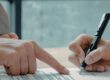 Person signing a will with legal documents and family photos on desk.